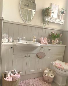 a white bathroom with pink rugs and accessories on the floor in front of a mirror