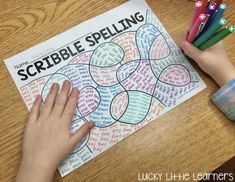 a child's hands holding colored crayons next to a printable scribble spelling game