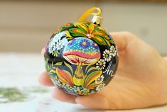 a hand holding an ornament with flowers and mushrooms painted on it's side