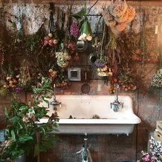 an old sink is surrounded by flowers and other things in the room that are hanging on the wall