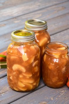 three jars filled with food sitting on top of a wooden table next to carrots