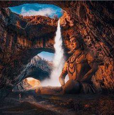 a man sitting in the middle of a cave with a waterfall coming out of it