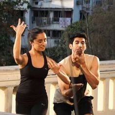 a man and woman standing next to each other with their hands in the air as they look at something