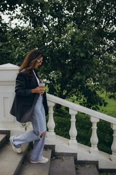 a woman walking down some steps while looking at her cell phone and holding a cup