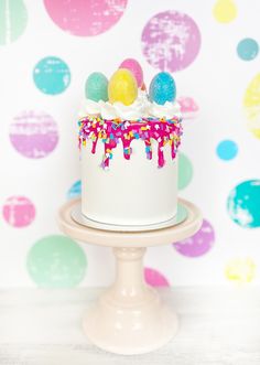 a white cake with sprinkles and eggs on top sitting on a stand