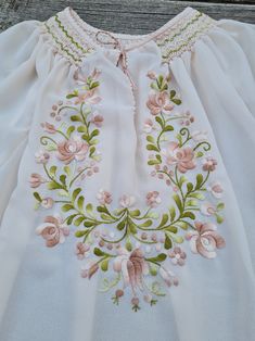 a white dress with pink flowers and green leaves on the chest, sitting on a wooden surface