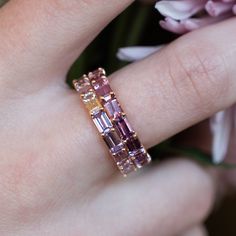 a close up of a person's hand with a ring on it and flowers in the background