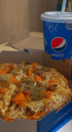 a pizza in a box next to a pepsi cup