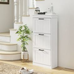 a white cabinet next to a stair case and potted plant in a room with wooden floors