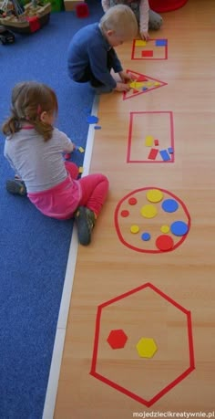 two children playing with matching shapes on the floor in a play area at a child's school