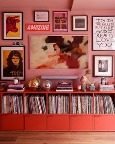 there are many records on the shelf in this room with pink walls and pictures above it