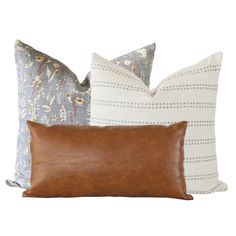 three pillows in different colors and patterns on a white background, each with a brown leather pillow