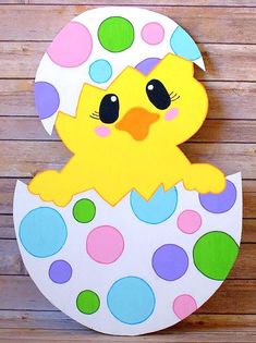 a painted wooden sign with a chick in an egg shell on a wood background that has multicolored polka dots