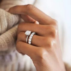 a woman's hand with two engagement rings on her finger and the other hand holding an engagement ring