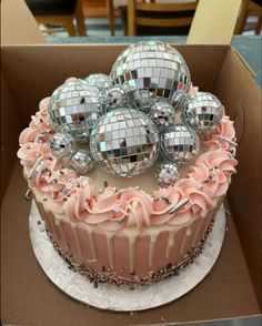 a cake with pink frosting and silver disco balls on top in a cardboard box