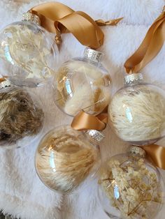 six glass ornaments with gold ribbons on a white blanket