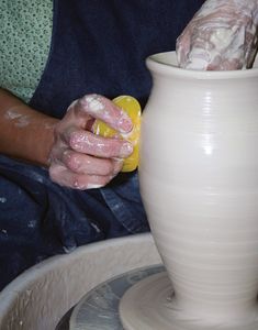 a person is making a vase out of clay with one hand and the other holding an object