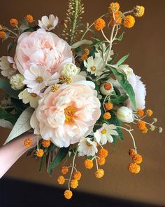 a bouquet of flowers is being held by someone's hand in front of a brown wall