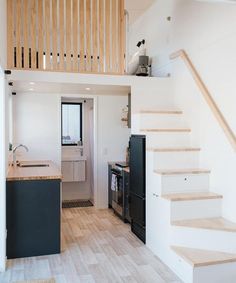 a kitchen and stairs in a small room with white walls, wood flooring and black appliances