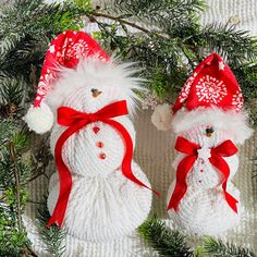 two knitted snowmen with red hats and bows on their heads hanging from a christmas tree