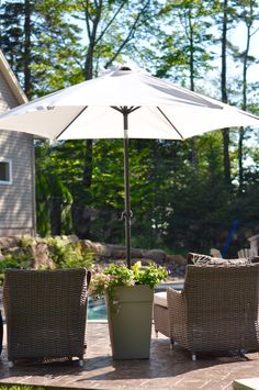 two wicker chairs and an umbrella are sitting on a patio near a pool in front of a house