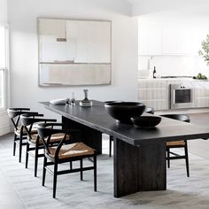 a dining room table with black bowls on it and chairs in front of the table