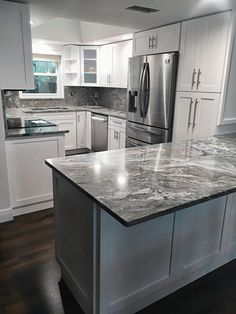 a large kitchen with white cabinets and marble counter tops, stainless steel refrigerator and dishwasher