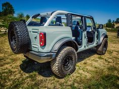 a light blue jeep parked on top of a grass covered field