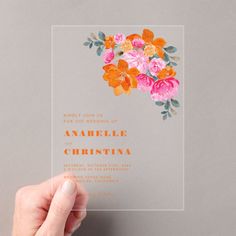 a person holding up an orange and pink flower on a clear card with the words happily join us for the wedding of