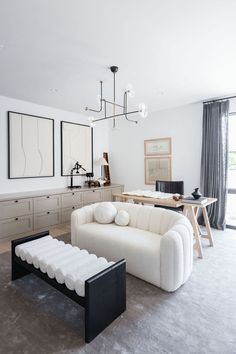 a living room filled with white furniture and art on the wall above it's windows