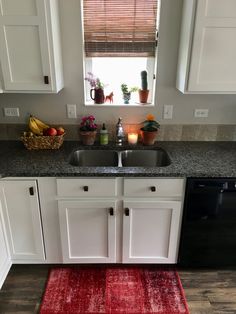 a kitchen with white cabinets, black appliances and a red rug in front of the sink