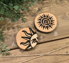 two wooden coasters with designs on them sitting next to a plant and another piece of wood