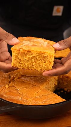 two hands holding a piece of cornbread in a skillet