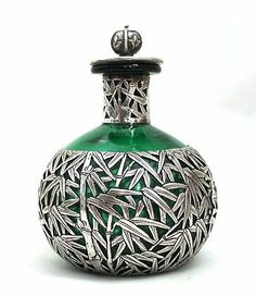 a green glass bottle with silver designs on it's top and bottom, in front of a white background