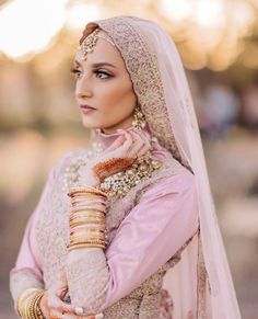 a woman in a pink outfit and gold jewelry poses for the camera with her hand on her arm