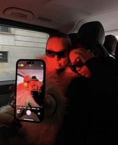 a man and woman taking a selfie in the back seat of a car with their cell phone