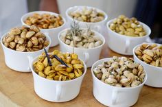 seven white cups filled with nuts sitting on top of a wooden table next to each other