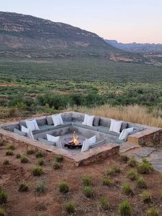 an outdoor fire pit surrounded by rocks in the middle of a field with mountains in the background