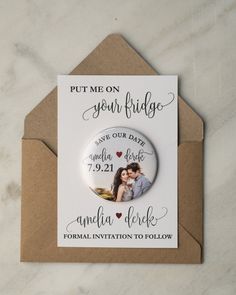 a wedding save the date magnet on top of an envelope with a button that says, put me on your fridge