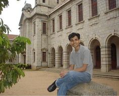 a young man sitting on top of a stone bench in front of a large building