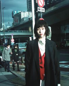 a woman in a black jacket and red shirt is standing on the street with other people