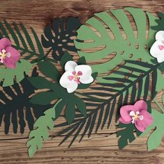 paper flowers and leaves cut out on a wooden surface with text overlay that reads, make your own tropical flower