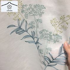 someone is stitching on the side of a white shirt with blue and green flowers