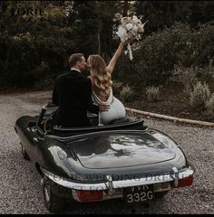 a bride and groom are sitting in the back of a convertible car with their hands up