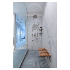 a bathroom with marble walls and flooring, shower head mounted to the wall next to a wooden bench