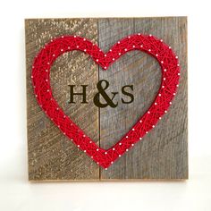 a wooden block with a red string heart and initials on it, in the shape of a heart