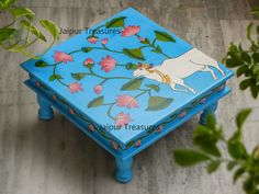 a small blue box with flowers and a cow painted on the lid is sitting next to a potted plant