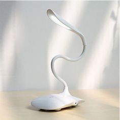 a white lamp sitting on top of a wooden table next to a plant in a vase