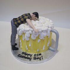 a birthday cake with a man laying on top of a mug filled with white frosting