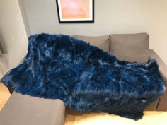 a couch with a blue fur covering it in front of a painting on the wall